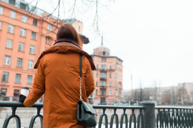 Bir kadın nehir ve şehir manzarasından zevk alır. Geri çekiliyor. Soğuk mevsimde yürür. Şehir manzarası. Rahatlama. Güvenlik için demir çitler.