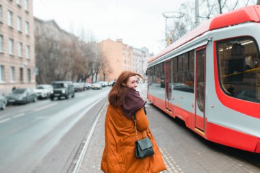 Bir kadın toplu taşımaya gider. Modern toplu taşıma. Şehir sokağı. Uzun, sıcak bir palto. Mutlu genç bir kadın. Tramvaya binen bir kadın. İş gezisi..