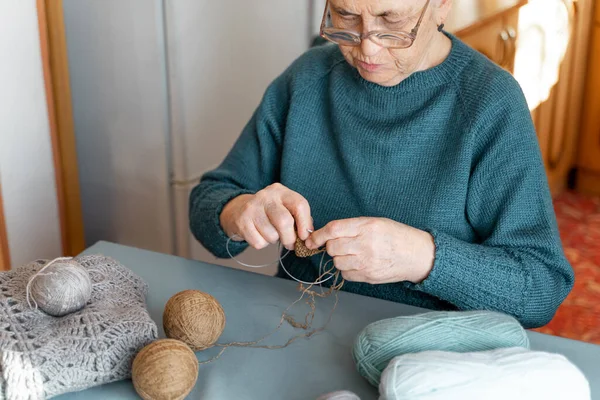 老太太坐着织毛衣 一位白发苍苍的老年妇女正在从事一种编织针头的业余爱好 桌上有毛线和一件针织夹克 — 图库照片