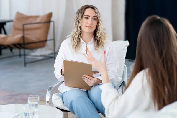 Kadın bir doktor hasta sorunlarını dinler, elinde bir dosya. Profesyonel psikolojik yardım. Doktor ve hasta oturuyorlar. Psikoterapist danışmanlığı