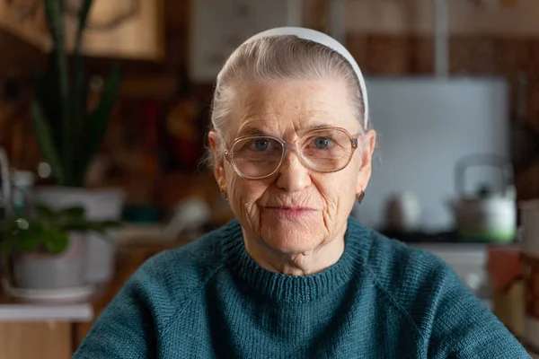 一个戴着大眼镜的老太太的画像 在家里的厨房里 看着相机 头上有一条灰色头发的发带 — 图库照片