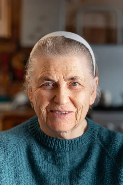 一位80年代快乐的老年妇女的脸他笑着看着摄像机 一个穿着针织绿色夹克 头发灰白的老妇人的画像 背景中厨房的水泡图像 — 图库照片