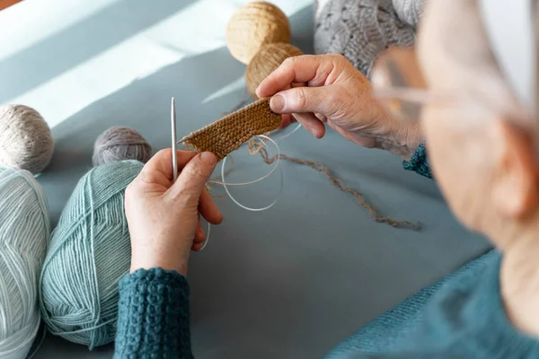 编织一位穿着针织冬季夹克的老妇人 她喜欢坐在桌旁编织 在舒适的冬天 顶部视图 桌上摆满了蓝色 棕色和灰色的针织线团 — 图库照片