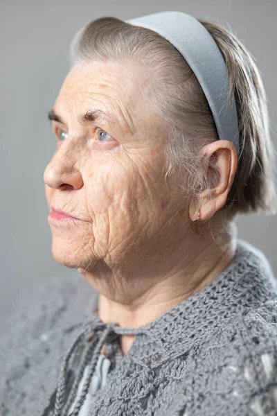 一个穿着针织灰色夹克 头发灰白的老年妇女的画像 祖母的画像 头上是一根灰色的发带 转头看 — 图库照片