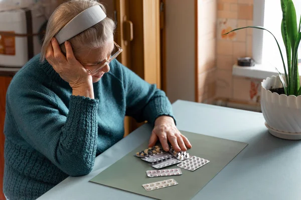一位悲伤的老妇人正坐在一个房间里看大量的药品 一位老妇人得了许多病 需要治疗 老年人的健康概念 — 图库照片