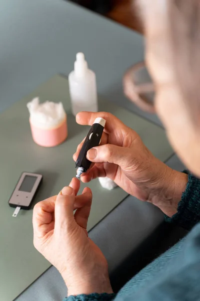 用一个用来测量血糖的柳叶刀刺穿你的手指 老年人中的糖尿病 桌上有胶粘剂 医用棉垫和过氧化氢 从后面看 — 图库照片