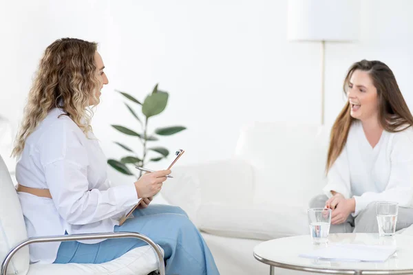 Konsültasyonda uzman kadın psikolog. Klinikteki randevusuna gülen kadın müvekkil.