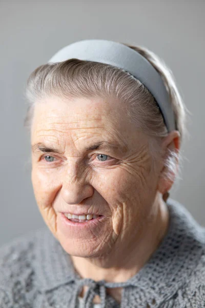 一个笑着的老年妇女的画像 一个白发苍苍的退休者 灰色背景 一个穿着针织夹克的祖母的画像 转头看 — 图库照片
