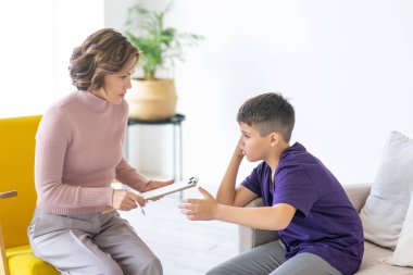 İlgili ve sempatik kadın psikoloğu genç oğlanı dinler. Not defterine not düşmüş. Ruh Sağlığı.