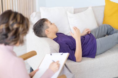 Sorunu için endişelenen genç çocuk kanepede yatıyor. Rahat klinikte psikoterapi görüyor. Akıl sağlığı. Önplanı bulanık olan bir psikolog..