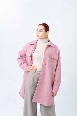Pembe ceketli, büyük düğmeli ve gri pamuklu pantolonlu kızıl saçlı bir Asyalı kadın. Büyük göğüs cepleri. Uzaklara bakıyorum..