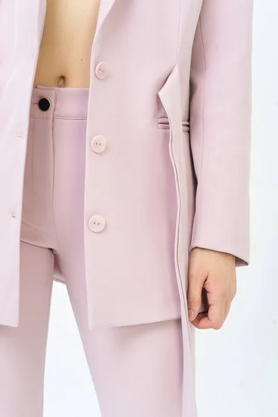 Close-up of belly of a woman in a pink suit, jacket and pants. Black button on the pants. A woman athletic body. Light background.