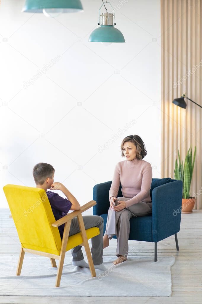 Middle-aged woman psychologist accepts teenager in light cozy office. Vertical image.