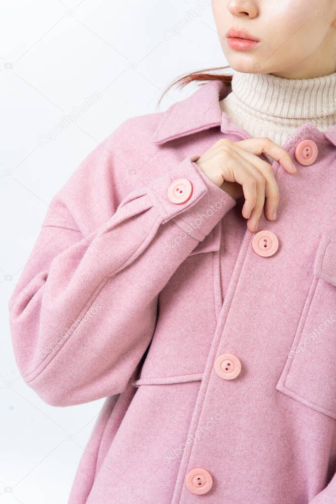 The sleeve of a thick women warm pink coat with large buttons. A woman in a turtleneck is buttoning her coat. White background.