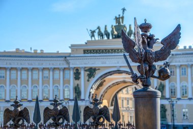 Kış Sarayı 'ndaki Alexander Sütunu' nun çitlerinde çift başlı kartal ve Saray Meydanı Zafer Kemeri manzarası (bulanık odak), St. Petersburg, Rusya