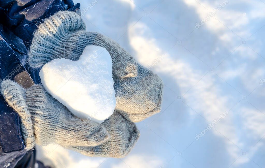 A heart made of snow lying on his hands in knitted mittens