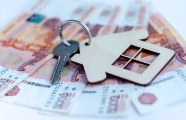 Rus parasının üzerinde duran ev şeklinde anahtarlığı olan bir anahtar. Finans, yatırım, tasarruf ve nakit kavramı.