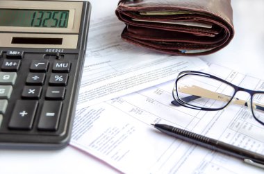 Calculator, glasses, wallet and pen are on utility bills.