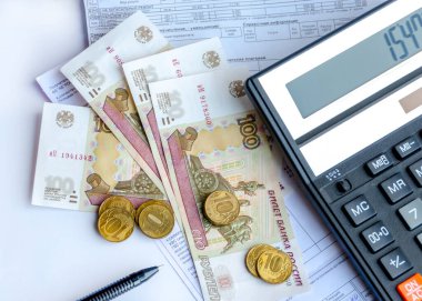 A calculator, Russian money, coins and pen are on utility bills, electricity.