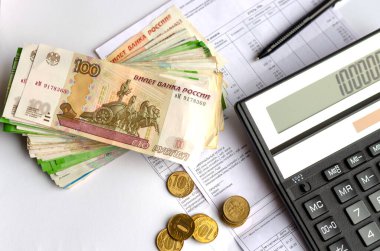 A calculator, Russian money, coins and pen are on utility bills, electricity.