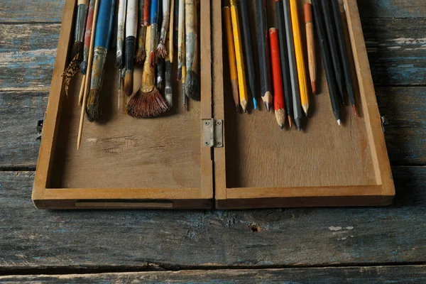           Eski ahşap bir tezgahın üstündeki kutuda fırçalar ve renkli kalemler..                     