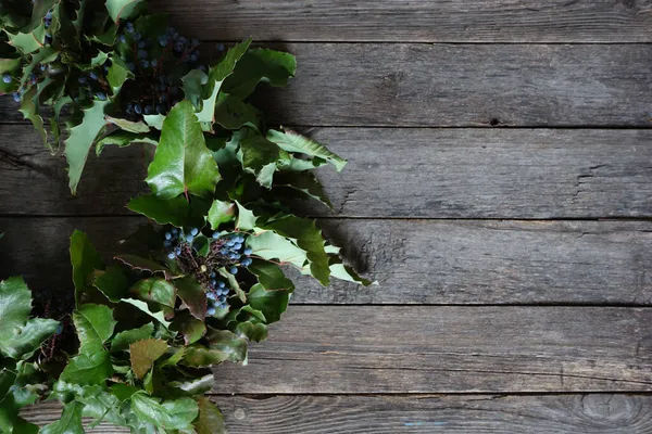 Yıllanmış ahşap arka planda mavi böğürtlenli kutsal yapraklardan yapılmış kırsal Noel çelengi. Mahnia aquiflium. Noel 'i kutlamak.