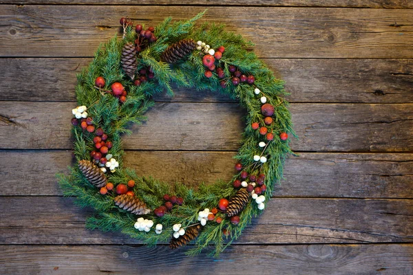         ,       .  Köknar kozalaklarıyla, böğürtlenlerle ve elmalarla eski ahşap arka planda ardıç dallarından yapılmış Rustik Noel çelengi. Noel 'i kutlamak..