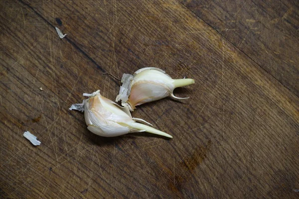 Kahverengi bir tahta üzerinde iki dilim soyulmamış sarımsak..