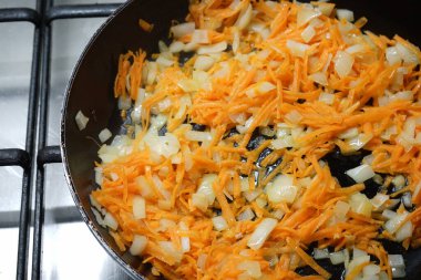 Soğan ve doğranmış havuç kızartma tavasında kızartılır. Soğan ve havuçlu dökme demir tava gaz ocağında..