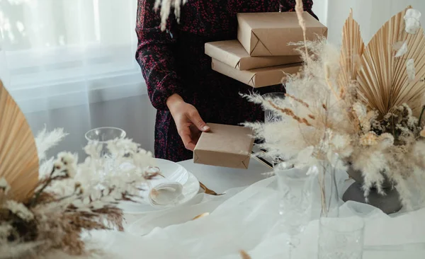 認識できない女性クリスマスディナーパーティーのテーブルを設定します 少数のクリスマスプレゼントを保持し 自宅で新年のお祝いのために飾られたテーブルの上に置くドレスの匿名の女性 — ストック写真