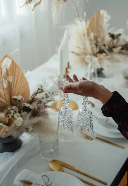 クリスマスディナーテーブルを自宅に設置する匿名の女性 2つの水晶ガラスを保持し エレガントな雑草や誕生日ディナーパーティーのためのテーブルを準備女性の手の写真を閉じます — ストック写真