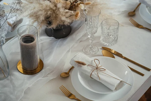 Decorated Dining Table for Weeding Lunch in a Restaurant.High angle view of a luxury table set up with white plates, crystal glasses, napkins, golden eating utensil, candle and flower arrangement.