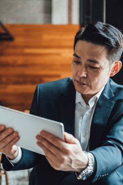 Yakışıklı Asyalı İş Adamı Kafe 'de Belgeler Okuyor. Mavi takım elbiseli ciddi bir iş adamı büyük pencerelerin yanındaki kafede otururken iş raporlarını tutuyor ve analiz ediyor..