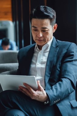 Yakışıklı Asyalı İş Adamı Kafe 'de Belgeler Okuyor. Mavi takım elbiseli ciddi bir iş adamı büyük pencerelerin yanındaki kafede otururken iş raporlarını tutuyor ve analiz ediyor..