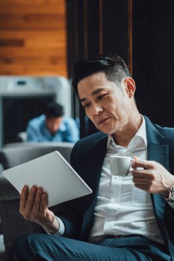 Yakışıklı Asyalı İş Adamı Kafe 'de Belgeler Okuyor. Mavi takım elbiseli ciddi bir iş adamı büyük pencerelerin yanındaki kafede otururken iş raporlarını tutuyor ve analiz ediyor..