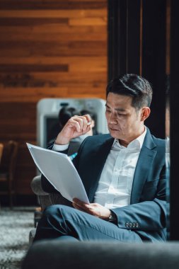 Yakışıklı Asyalı İş Adamı Kafe 'de Belgeler Okuyor. Mavi takım elbiseli ciddi bir iş adamı büyük pencerelerin yanındaki kafede otururken iş raporlarını tutuyor ve analiz ediyor..