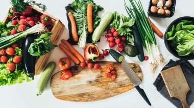 Sağlıklı Yeme: Beyaz Mutfak Masası Taze Organik Sebzelerle Dolu. Tahta sandıkta renkli sebzelerin fotoğrafının hemen üstünde kesim tahtası ve mutfak bıçağının yanındaki masada..