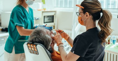 Dişçi Kliniğindeki İsimsiz Olgun Bir Adam Diş Deliğini Doldurmak İçin Diş Tedavisine Gidiyor. Erkek hasta dişçi koltuğunda otururken ve dişlerini düzeltirken, dişçi asistanı dişçi kliniğinde dişçiye diş aleti verirken,.