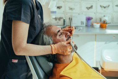 Olgun Adam 'ın dişçi muayenehanesinde dişçi prosedürü uygulaması. Tanımlanamayan dişçi kadının, diş sağlığı kliniğindeki diş dolgusunu tedavi etmek için dişçi matkabı kullanan turuncu eldivenlerini teslim ederken fotoğrafını çek..