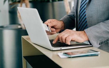 Havaalanında kredi kartı satın alan isimsiz bir işadamı bilgisayarını kullanan bir adamın fotoğrafı ve havaalanı terminalinde beklerken internet rezervasyonu yapmak ya da vergi ödemek için kredi kartı kullanıyor..