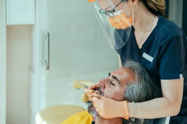 Dişçi Kliniğindeki Olgun Adam Diş Sağlığı Tedavi Ediyor Bir Diş Deliğini Bileşikle Doldurmak İçin. Erkek hasta, dişçi koltuğunda ağzı açık oturuyor ve COVID-19 sırasında diş hekiminde dişçiye diş tedavisi yaptırıyor..