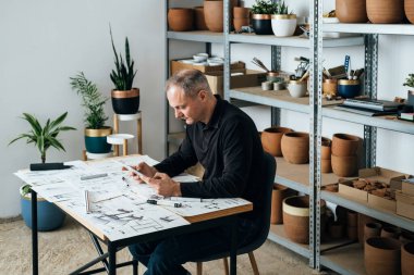 Mutlu Tasarımcı, iş yerinde dijital tablet kullanıyor. Gülümseyen mobilya tasarımcısı masasında oturmuş modern bir masa tasarımının taslakları ve taslaklarıyla dijital tabletinde analiz ediyor..