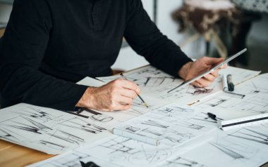 Ofisinde Dijital Tablet ve Planlar üzerinde çalışan isimsiz bir tasarımcı. Mobilya tasarımcısı ellerin dijital tabletini kullanırken çizim yaparken ve masasında otururken resmini kapat..