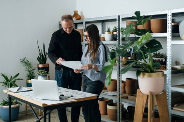Başarılı Mimarlar Takımı yeni bir iş projesinde birlikte çalışıyor. Kadın ve erkek mühendisler, ofislerinde dizüstü bilgisayar ve planlar kullanarak bir proje tasarımı üzerinde tartışıyorlar..