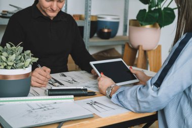 Tanımlanamayan Mobilya Tasarımcısı Ekibi El Yapımı Çiçek Saksısı Tasarımı Üzerinde Birlikte Çalışıyor. Kadın yeni proje tasarımı için dijital tablet kullanırken, erkeğin ellerinin masaya bir plan çizdiği fotoğrafı kapat.