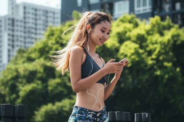 Spor Giyim 'de gülümseyen kadın açık havada cep telefonu kullanıyor. Şehirde koştuktan sonra akıllı telefon uygulamasında müzik dinleyen ve spor yapan mutlu bayan sporcu..