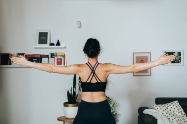 Sabahları kollarını ve omuzlarını uzatan isimsiz bir kadın. Evde yoga yapan, kolları açık duran ve nefes alma egzersizi yapan tanınmayan bir kadının arka görüntüsü..