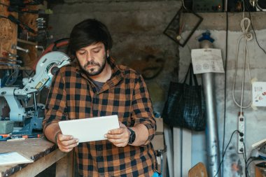 Ciddi Marangoz atölyesinde dijital tablet kullanıyor. Marangozluk atölyesinde tabletinde bir şeyler okuyan yakışıklı bir adam..
