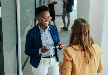 Sayısal Tablet Tutan ve İsimsiz Kadın İş Arkadaşıyla Konuşan Mutlu Afro-Amerikalı İş Kadınları