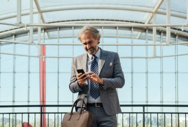 Havaalanında dikilirken cep telefonu kullanan gülen iş adamı.